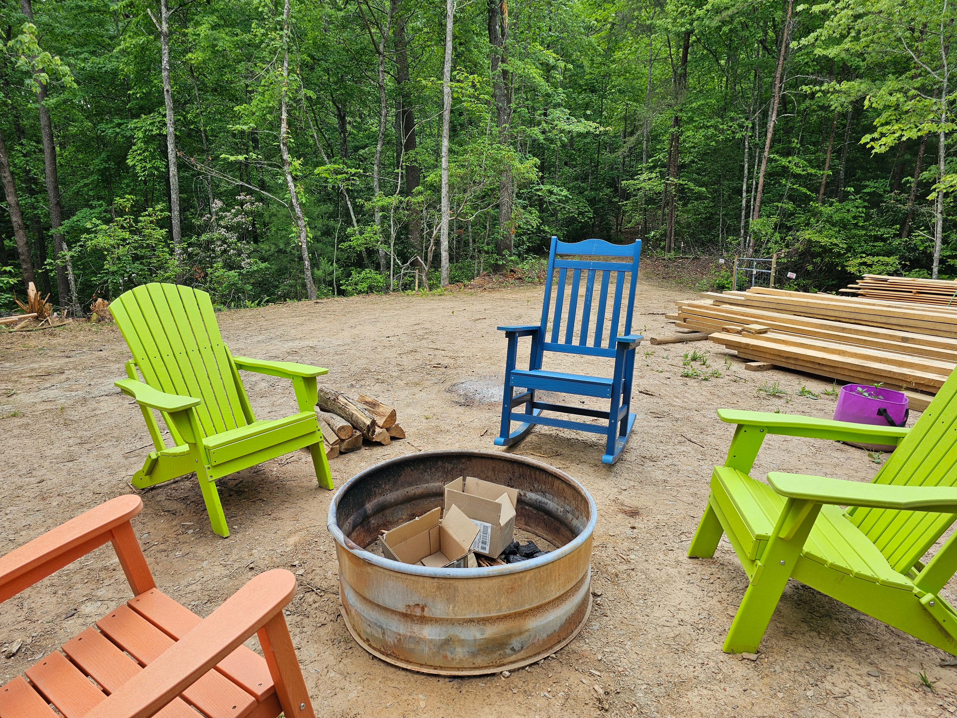 Outdoor fire pit with Adirondack chairs in a dark forest at night